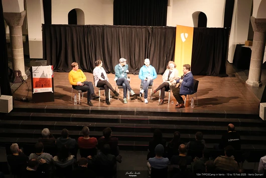 A panel discussion at WebCamp Venlo 2025 featuring six experts on stage discussing the challenges and sustainability of open-source financing. The engaged audience listens attentively.