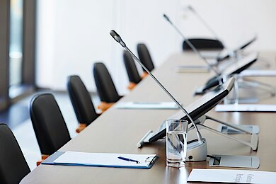 Modern conference room with a long table, equipped with microphones, tablets, writing pads and glasses of water - ready for a board meeting or a business meeting.