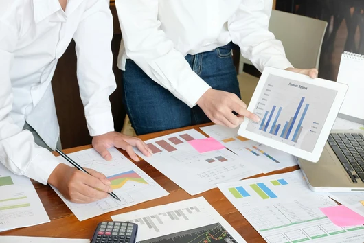 Two office workers in white shirts stand at a table with business papers