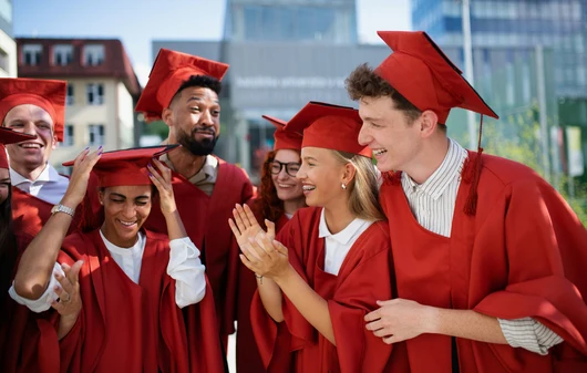 Happy graduates in red gowns stand in a group and talk