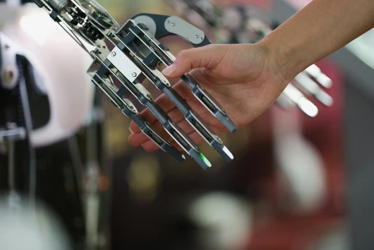 Eine menschliche Hand hält die mechanische Hand eines Roboters. Dieses Bild symbolisiert die Interaktion zwischen Mensch und Technologie sowie die Zusammenarbeit zwischen Mensch und künstlicher Intelligenz.