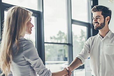 Geschäftlicher Handschlag zwischen Bewerberin und Arbeitgeber in moderner Büroumgebung.