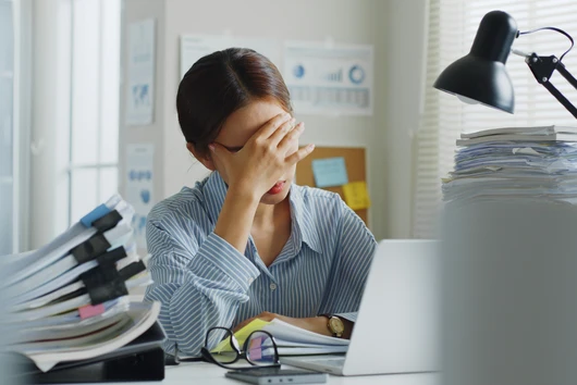 Frau im Büro am Schreibtisch hält die Hände vor das Gesicht