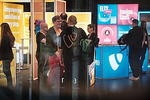Networking am TYPO3-Stand während der T3CON25 Menschen, die während der T3CON25 am TYPO3-Stand interagieren und sich vernetzen, umgeben von beleuchteten Displays und farbenfrohen Markenpanels.